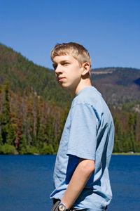 Boy looking away while standing against lake at forest