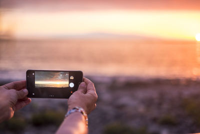 Cropped hands photographing sea with smart phone at sunset