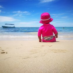 Rear view of baby girl sitting on sand at beach