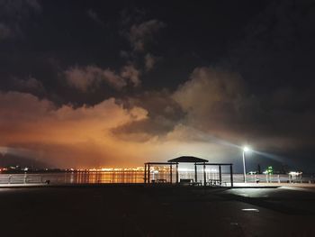 Illuminated pier over sea against sky at night