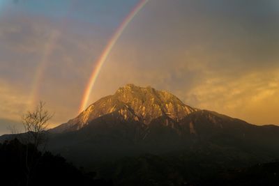 Scenic view of rainbow over mountains against sky during sunset