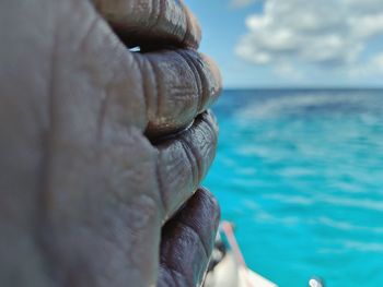 Close-up of human hand against sea