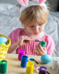 Little girl in easter bunny ears painting colored eggs. easter celebration and craft concept.