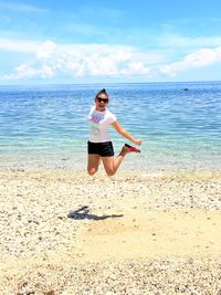 Young woman jumping at beach against sky