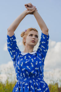 Portrait of young woman standing against blue sky