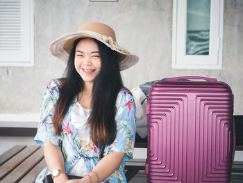 Smiling woman wearing hat sitting by luggage