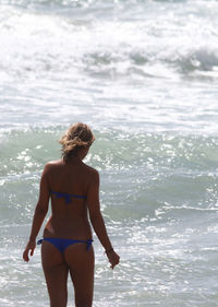 Rear view of woman wearing bikini standing in sea during sunny day