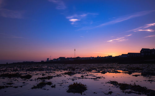 Silhouette of city by sea against sky during sunset