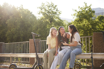 Young female friends spending time together outdoors and using phone