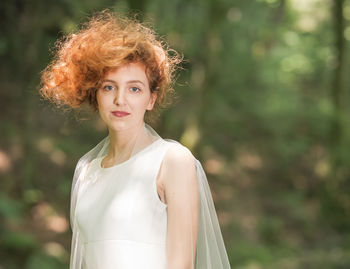 Portrait of young woman standing against trees