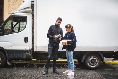 Young woman signing on smart phone while receiving package from male mover