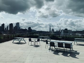 Empty chairs and tables in city against sky