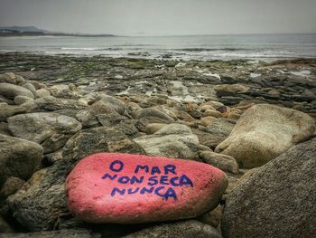Close-up of text on pebbles at beach against sky