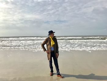 Man standing on shore at beach against cloudy sky