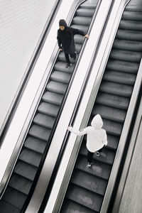 High angle view of man and woman wearing hooded shirts walking on escalators