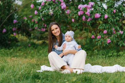 Charming mother and her little son are sitting on a blanket in spring in a blooming park