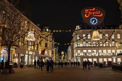 People on illuminated street amidst buildings at night