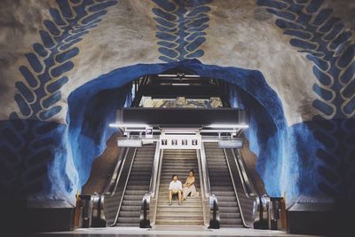 Low angle view of couple sitting on steps amidst escalator at railroad station