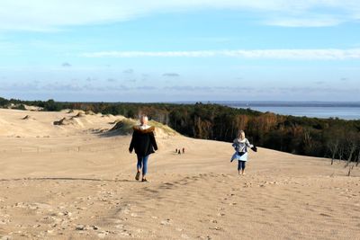 Rear view of people walking on land against sky