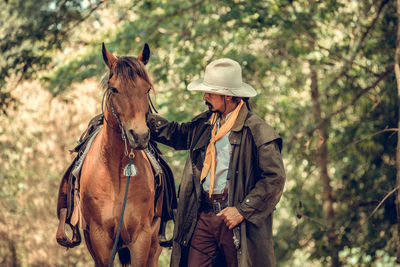 Man wearing hat walking with horse at forest