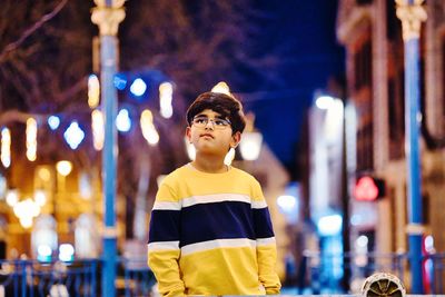 Portrait of boy standing against illuminated lights at night