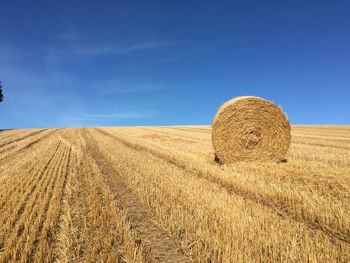 Hay bales on field against blue sky