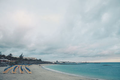 Lounge chairs and parasols arranged at beach against cloudy sky