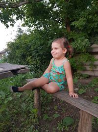 Cute girl sitting on wooden bench in yard