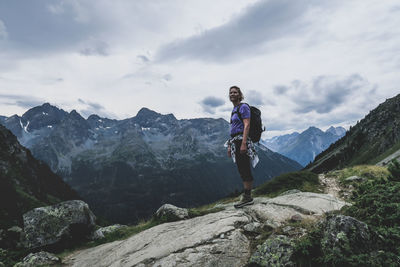 Low angle view of mid adult woman standing on mountain against cloudy sky