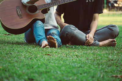 Low section of couple with guitars sitting on grass at park