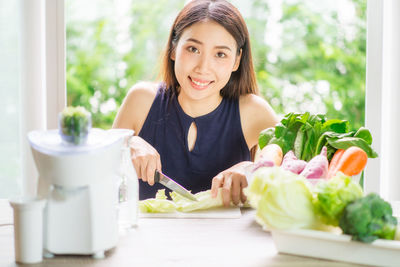 Portrait of smiling young woman cutting vegetables at home