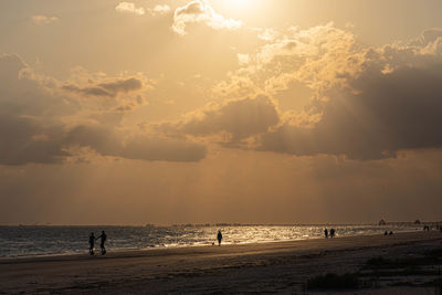 Silhouette people on beach against sky during sunset