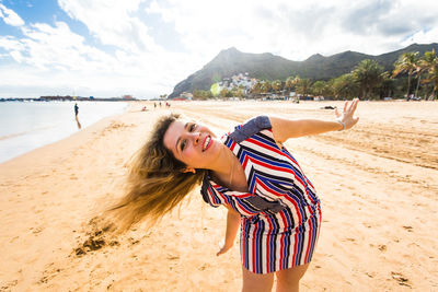 Young woman with umbrella on beach against sky