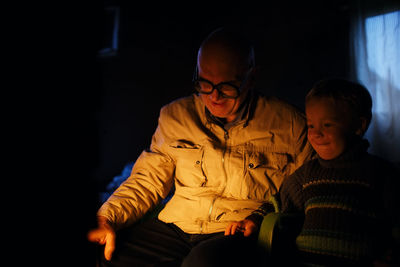 Smiling grandfather and grandson sitting in dark at home
