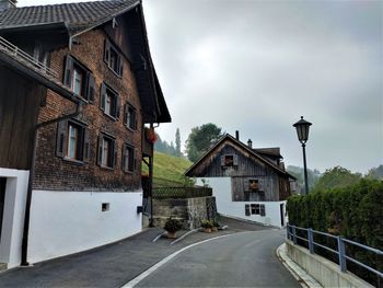 Road amidst houses and buildings against sky