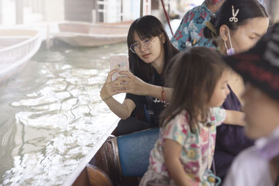 Young woman sitting in boat and taking photos with smart phone