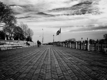 People walking on road against cloudy sky