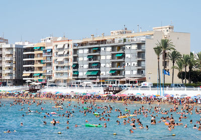 People swimming in sea against buildings at city