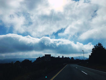 Cars on road against cloudy sky