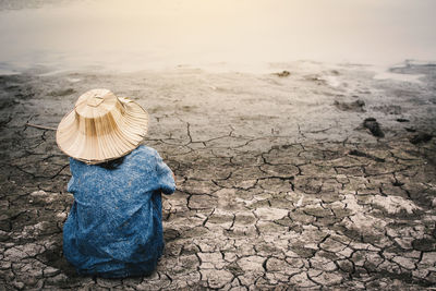 Rear view of girl sitting by pond on drought field