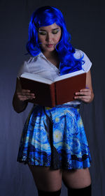 Young woman reading book against blue wall