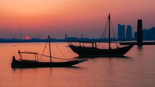 Sailboats moored on sea against sky during sunset