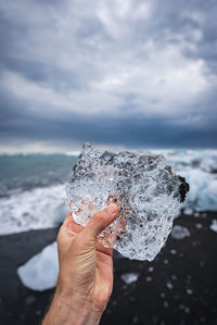 Cropped hand holding ice cream cone against sky