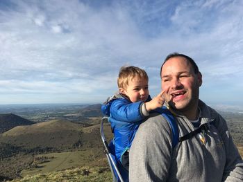 Father carrying baby while standing on mountain against sky