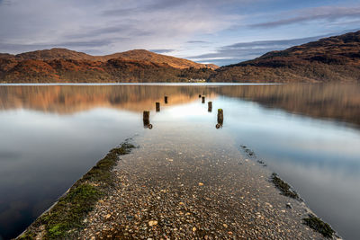 An old jetty on the shores of loch lomond, scotland with the mountains of loch lomond national park.