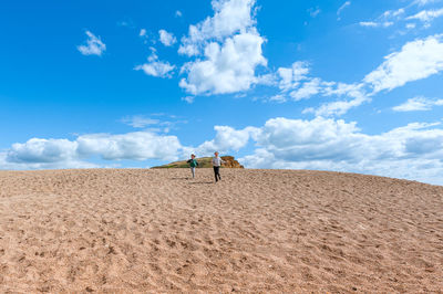 Low angle view of kids walking on sand dune against sky