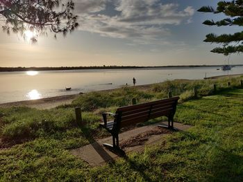 Empty bench by lake against sky