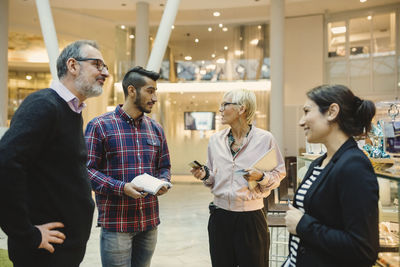 Mature businesswoman holding credit cards while discussing with colleagues in office