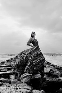 Full length of young woman on rock at beach against sky