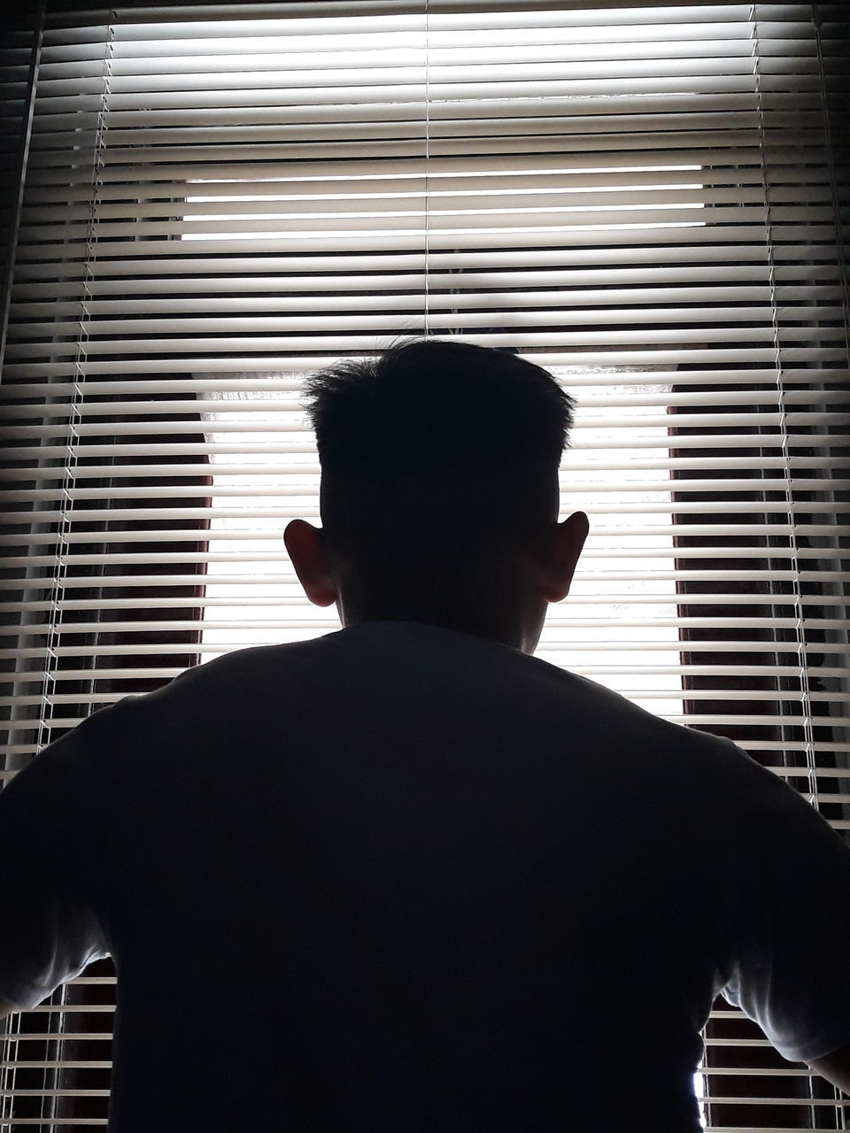 REAR VIEW OF MAN STANDING AGAINST WINDOW